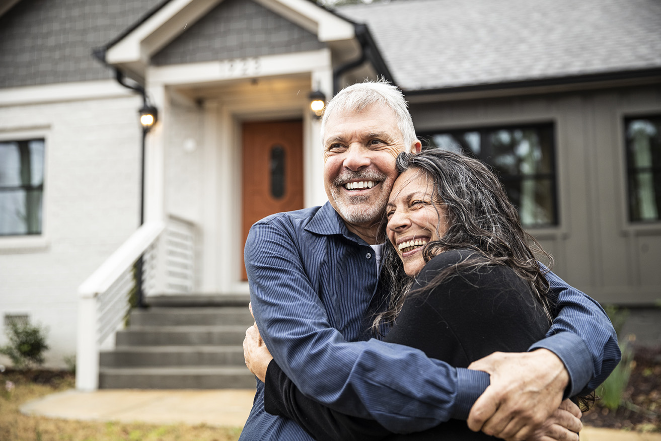 Couple embracing in front of their home.